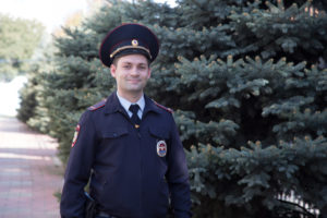 полицейский стоит возле елок и улыбается
